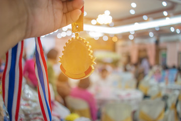 Businessman hands raised and holding gold medals with Thai ribbon against convention hall background to show success in business, Winners success award concept.