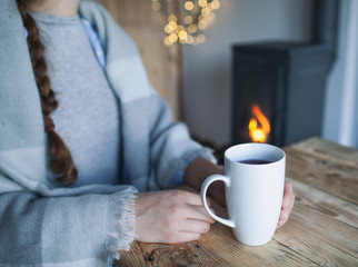 Woman with cup of coffee sitting by the fireplace and wooden table