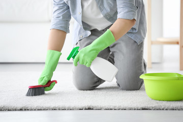 Man cleaning white carpet with brush in living room