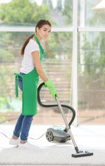 Woman cleaning carpet with vacuum near large window