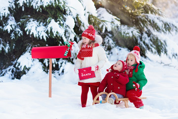 Children with letter to Santa at Christmas mail box in snow