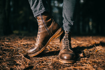 Odd woodcutter in vintage hipster masculine rough leather wooden boots standing in autumn forest on ground with dry orange spruce needles. Fall colors and mood concept. Sunny day outdoor at weekend.