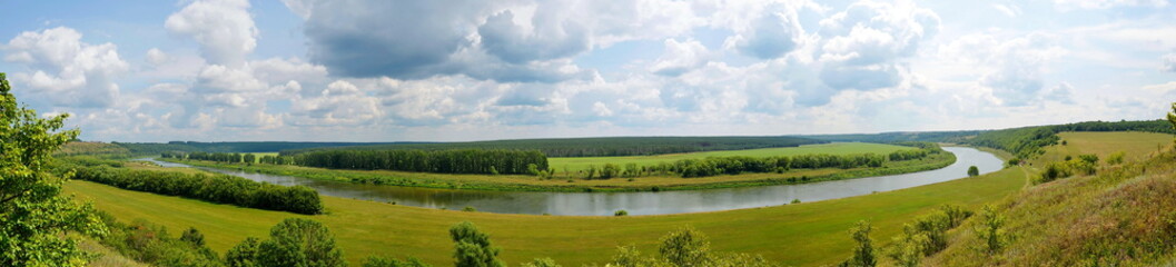 the riverbed from a height, a green field and lots of blue sky with clouds, landscape, panorama