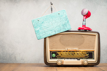 Retro wooden broadcast radio receiver with green eye light, studio microphone and aged signboard blank front concrete wall background. Listen music concept. Vintage instagram old style filtered photo