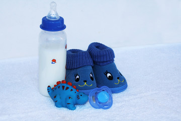 Set for newborn boy with baby milk, toy, pacifier, anti cute funny blue shoes on white background.