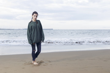 Young pretty woman standing alone on the beach near the sea, waiting for somebody in the ocean.