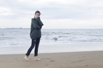 Young pretty woman standing alone on the beach near the sea, waiting for somebody in the ocean.