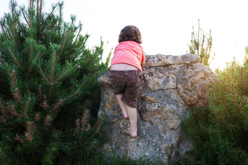 The boy climbs on the stone.