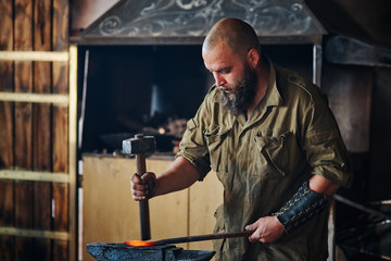 Fototapeta na wymiar Blacksmith working in the forge. Manufacture of parts and weapons from molten metal, using the hammer and anvil.