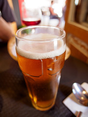 Close-up detail of a cold, tall glass of a dark yellow lager and foam at a restaurant. Vertical orientation. Valencia, Spain. Travel and drinks concept.