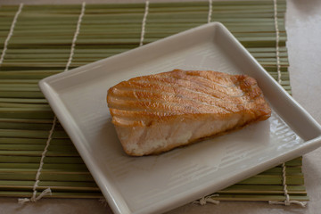 fried salmon ready to serve on white plate and bamboo mat