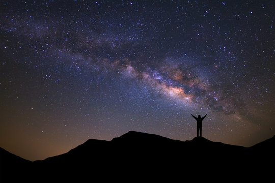 landscape with milky way, Night sky with stars and silhouette of a standing sporty man with raised up arms on high mountain.