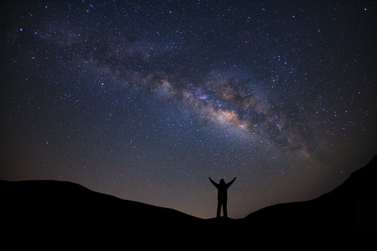 Panorama landscape with milky way, Night sky with stars and silhouette of a standing sporty man with raised up arms on high mountain.