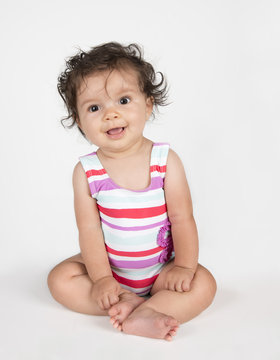Cute baby girl in striped swimsuit sitting on white background