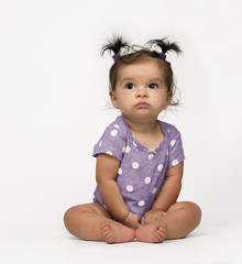 Sweet, serious baby girl sitting in polka dot onesie on white background