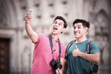 Fototapeta premium positive men tourists with suitcases are making selfie in unknown city