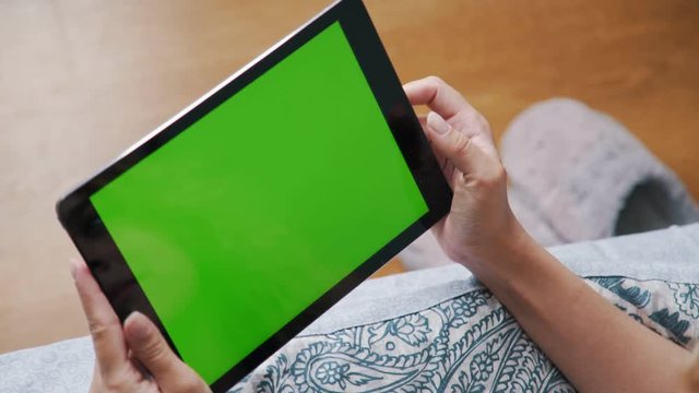 Tablet computer in female hands: touching the screen (touchscreen), browsing the Internet. Green screen. Gadgets and modern technology. Use of the tablet: in the frame only hands.