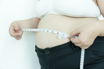 Woman measuring her waistline fat tummy with measuring tape on gray background.