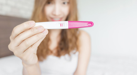 Selective focus Pregnancy test positive result on hand of smiling woman in her bedroom,Blurred background.