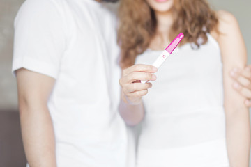 Selective focus happy couple hugging with positive pregnancy test in bedroom.