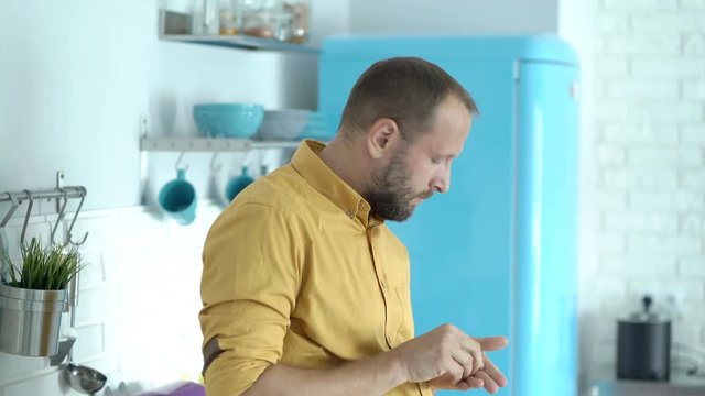 Man having painful headache while standing in his modern kitchen and takes painkiller
