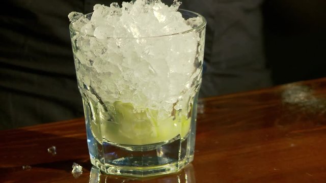 Caipiroska coktail. The barman adds ice to the glass with lime.