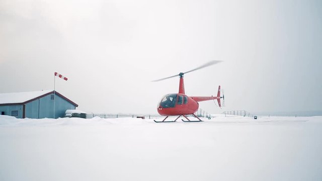 A red helicopter takes off in a snow-covered field.