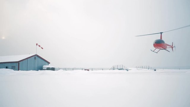 A red helicopter sits on a snow-covered field.
