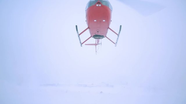 A red helicopter takes off in a snow-covered field.