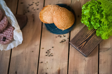 Cutlets for burgers lie on a wooden board with peas of pepper. Raw cutlets for burger. Pork and ground beef. Corn and green leaves and burger rolls.