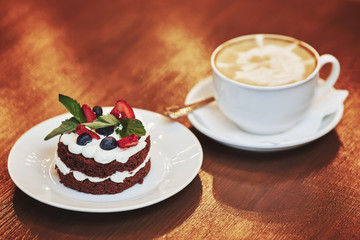 Chocolate cake with cream, berries and cup of latte coffee