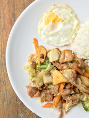 Thai spicy food : A plate of pork stir fry with vegetables and fried egg with rice in white dish on wooden table.  healthy dish.