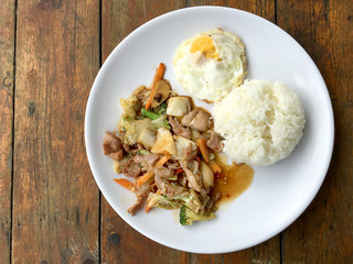 Thai spicy food : A plate of pork stir fry with vegetables and fried egg with rice in white dish on wooden table.  healthy dish.