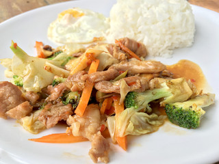 Thai spicy food : A plate of pork stir fry with vegetables and fried egg with rice in white dish on wooden table.  healthy dish.