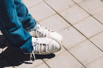 Women's feet in sneakers are standing on the sidewalk