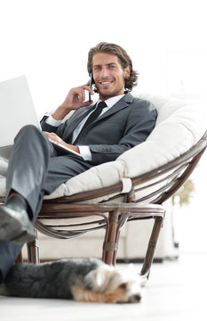 businessman talking on smartphone sitting in chair in his house