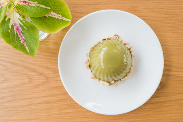 Green dessert  is made from green tea with red bean paste. In a white plate on the table .