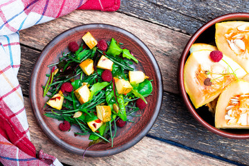 Warm pumpkin salad with raspberries and mixed leaf of arugula, chard, in brown plate on wooden rustic background. Top view.