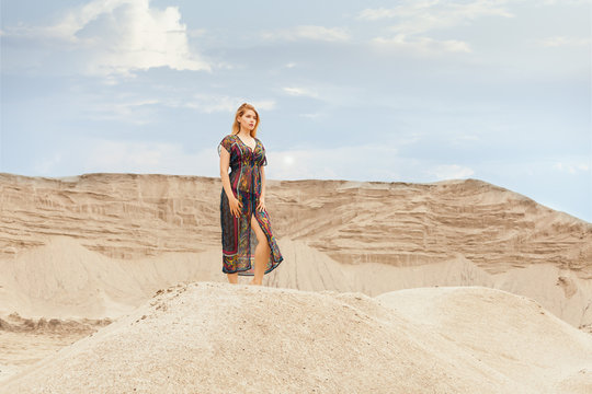 Woman in the desert among the dunes, she is dressed in a lightly gleaming dress.