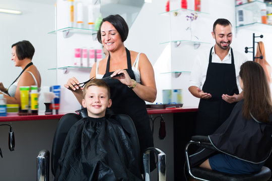 Glad kid sitting in chair and getting hair cut