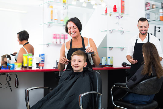 Happy kid getting hair cut by woman hairdresser