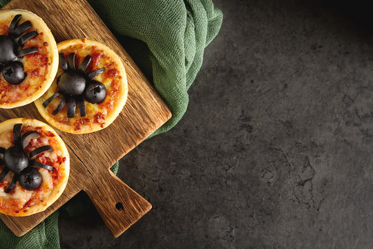 Italian homemade mini pizza with cheese, tomatoes, olives. Dark background. Halloween and spiders