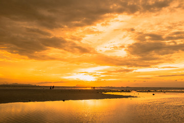 Golden scene on the beach at sunset. Group of tourists watching sunset at the coast.