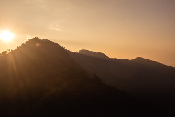 Sunset scene on hight mountain. Sunshine through the clouds. silhouette at the mountain.