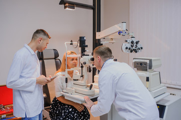 Young beautiful two doctors /eye specialist/optometrist in an ophthalmologic clinic examines a woman patient with biomicroscopy