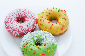 Green, yellow and pink Donuts with colored polka dots on a plate on a white background. Fried dough confectionery. Dessert food, snacks, sweets. National Doughnut Day.