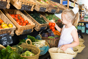 girl choosing vegetables in vegetable shop. on the signboard inscriptions in Catalan