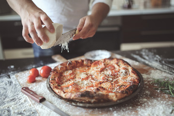 male hands rubbed cheese grated on pizza in home