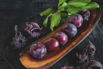 Beautiful ripe blue plums in sugar with dried hibiscus flowers on a wooden Board. Copy space.