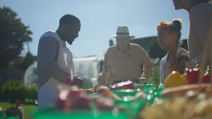  Cheerful man selling fresh fruit & veg to customers at outdoor summer market.